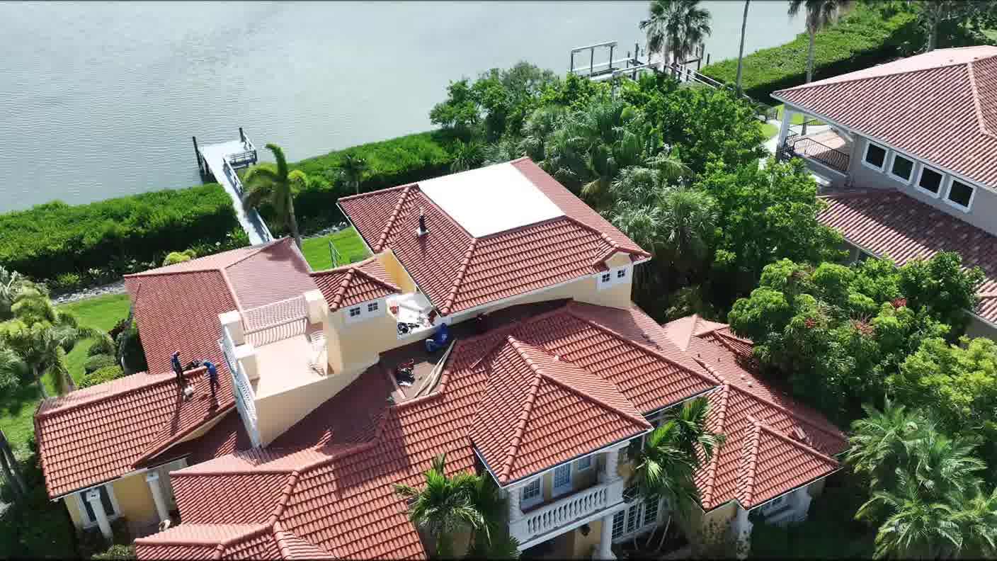 Wide aerial view of tile-roofed homes on the water with a dock