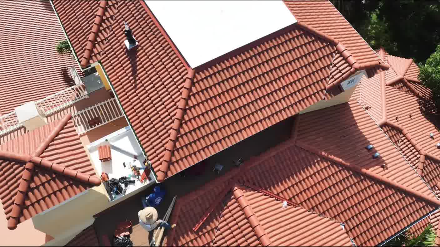Close aerial view of a barrel tile roof with roofers working on it