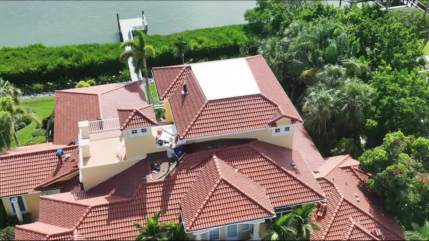 Aerial view of a tile-roofed home with a dock and open water behind it