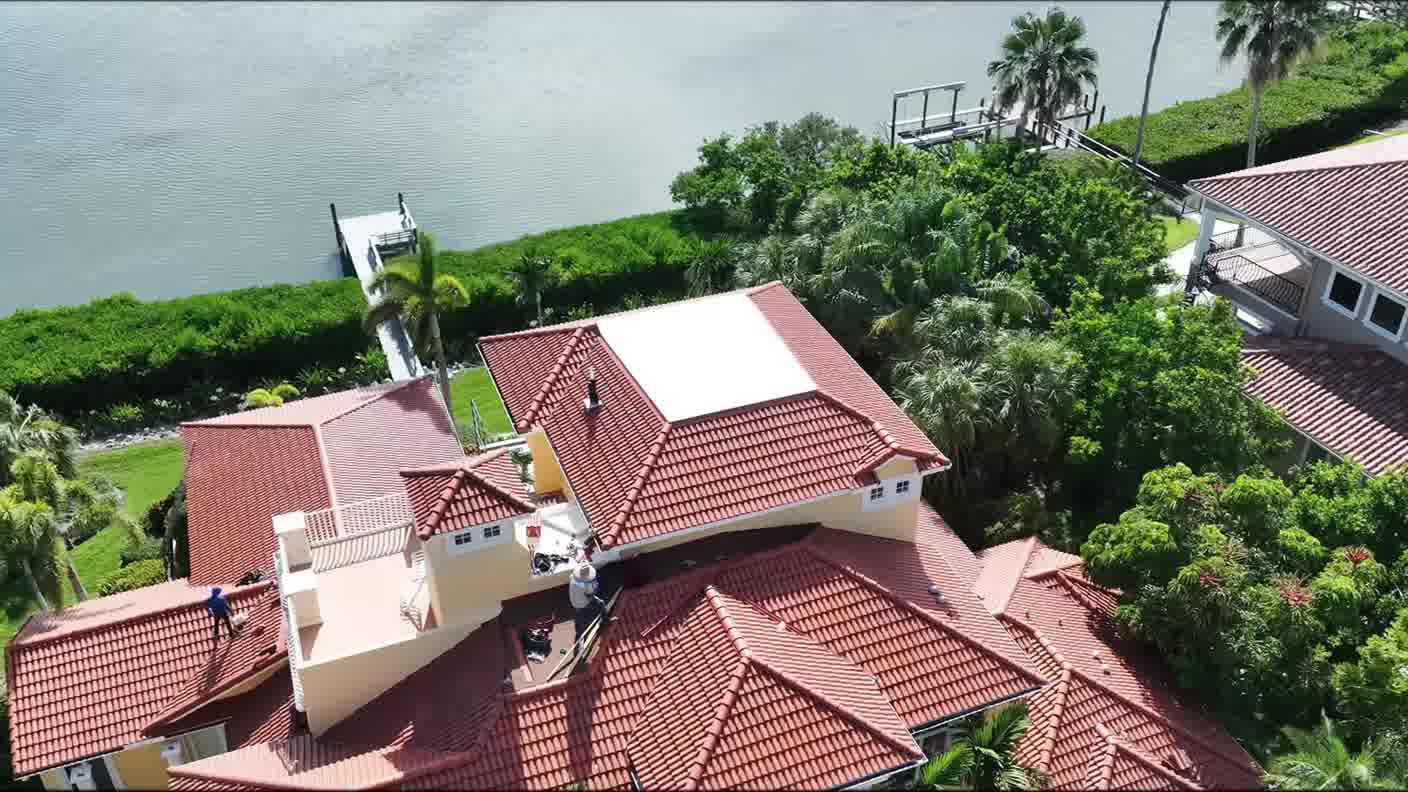 Aerial view of roofers working on a waterfront home with a dock and palms